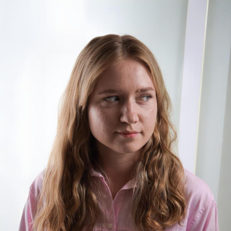 Junge Frau sitzt lächelnd in einem modernen Büro mit gemütlicher Atmosphäre und grünen Pflanzen im Hintergrund.