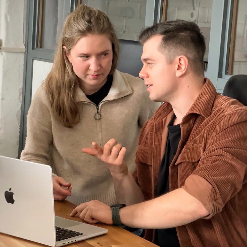 Eine Frau und ein Mann sitzen vor einem Laptop und diskutieren konzentriert über ein gemeinsames Projekt in einem modernen Büro.